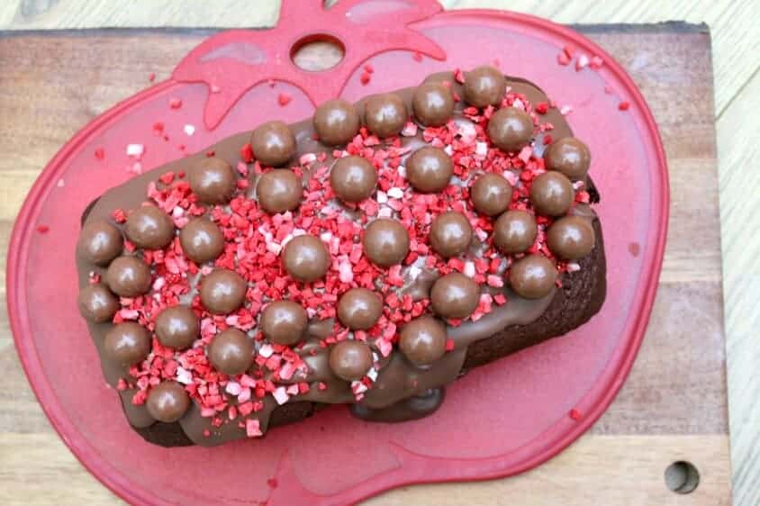 Overhead view of chocolate loaf cake decorated with Malteser balls and red strawberry pieces.