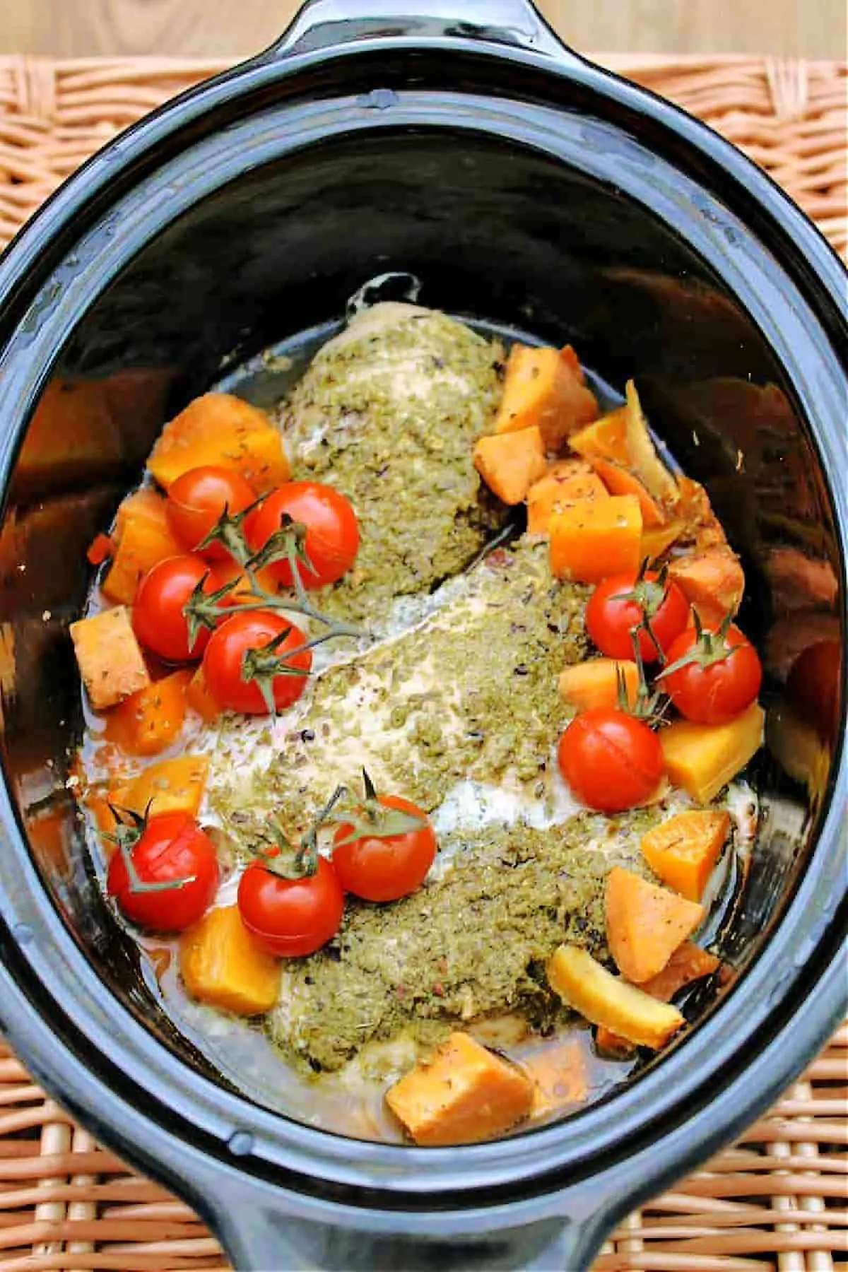 Slow cooker full of chicken with pesto on top, tomatoes and sweet potato chunks.