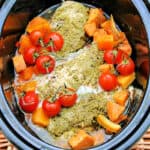 Slow cooker pot with chicken with pesto on top, tomatoes and sweet potato chunks.