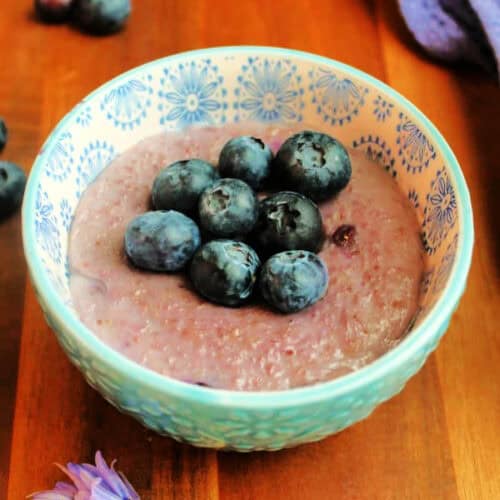Blueberry porridge topped with more blueberries in a patterned bowl.
