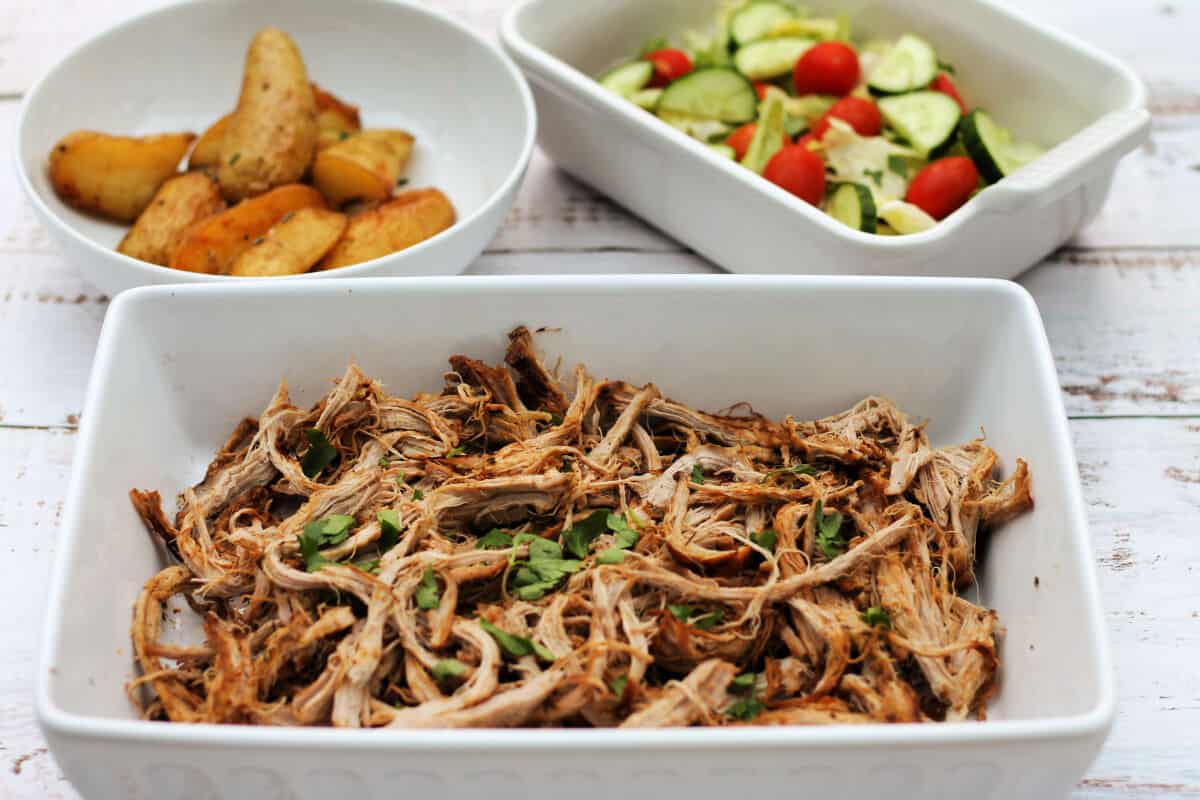 White bowl of pork in front, bowls of salad and potatoes at the back.