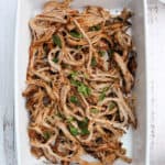 Shredded pork fillet in a white serving dish, with herb garnish.