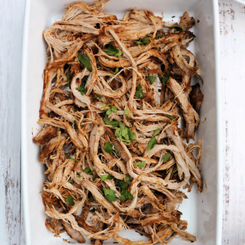 Shredded pork fillet in a white serving dish, with herb garnish.