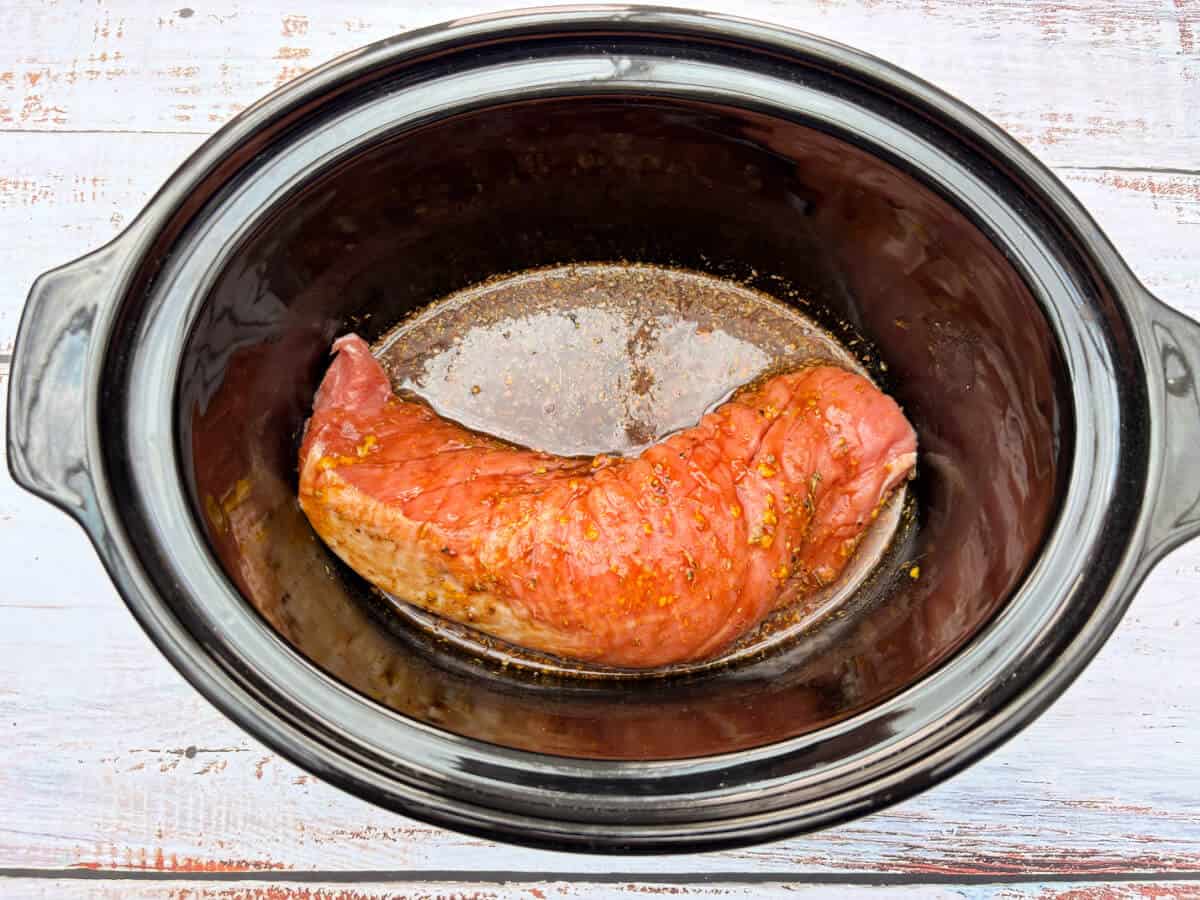 Pork fillet coated in marinade in slow cooker pot.