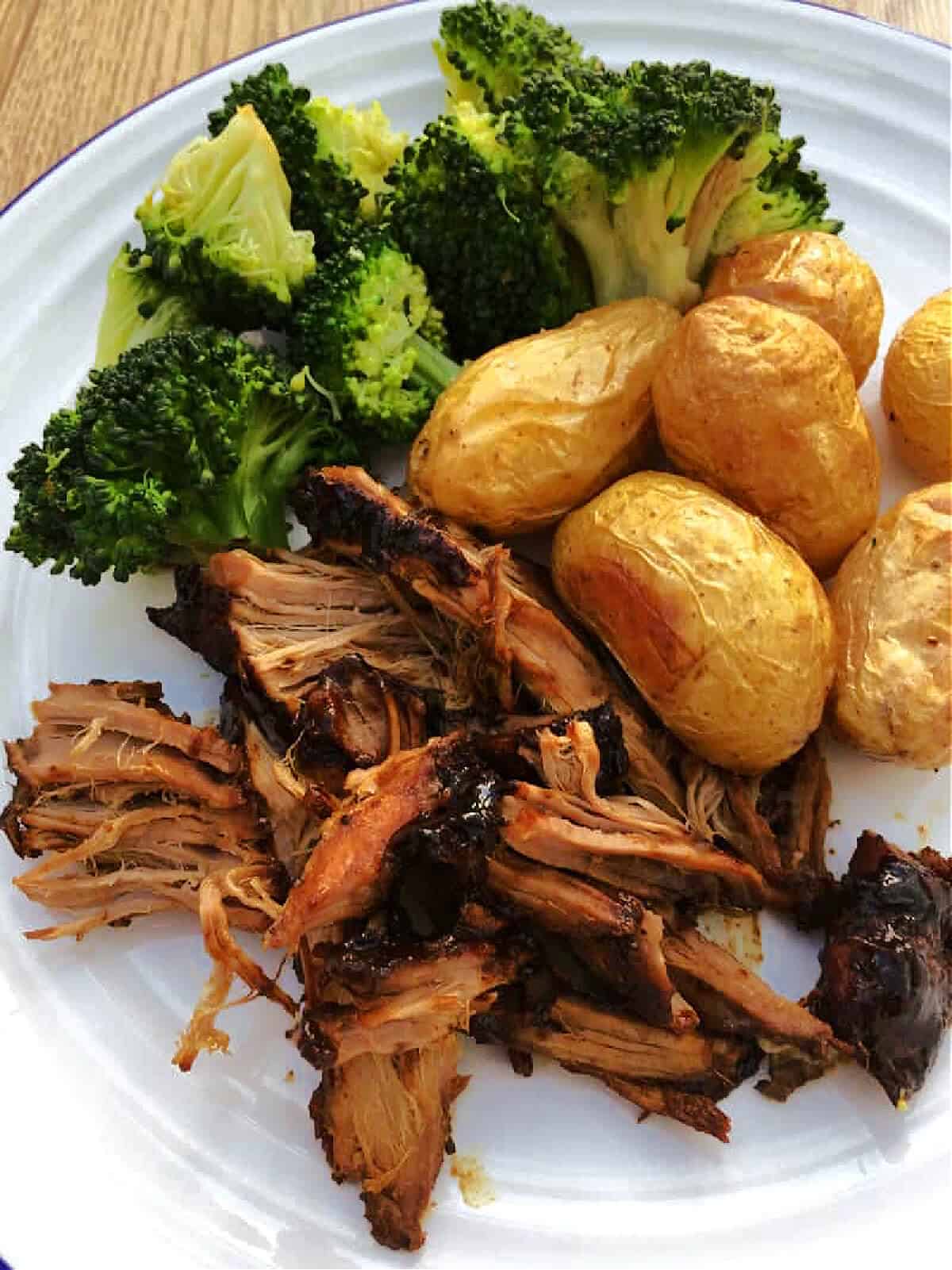 Shredded pork fillet served on a white plate with roasted new potatoes and broccoli.
