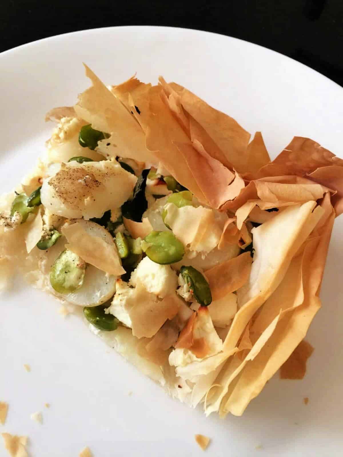 Portion of filo tart with feta and broad beans on white plate.