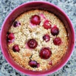 Round serving dish with baked oats studded with bright pink gooseberries.