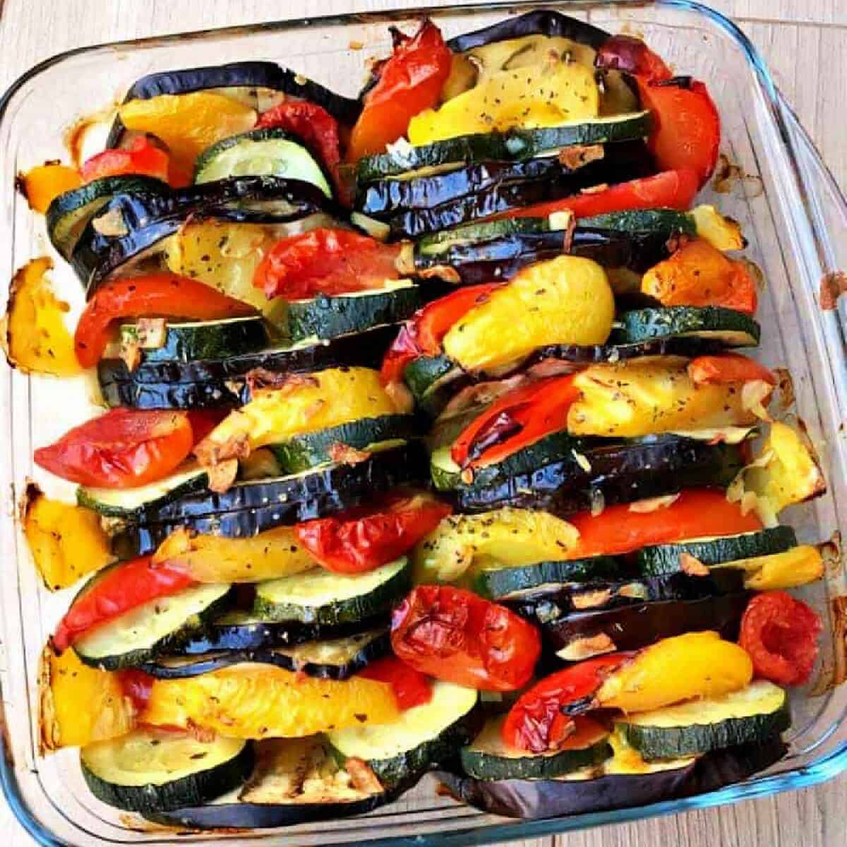 Peppers, aubergines and tomatoes in a pyrex dish, arranged in a pattern.