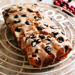 Close up of fruit-studded cranberry cake on cooling rack, with dripping icing.