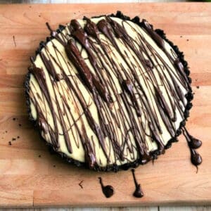 White chocolate tart with chocolate drizzle on wooden board.