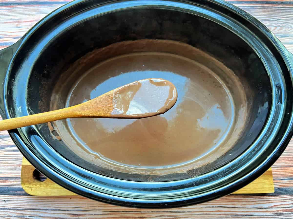 Thickened hot chocolate in slow cooker pot, coating a wooden spoon held above it.