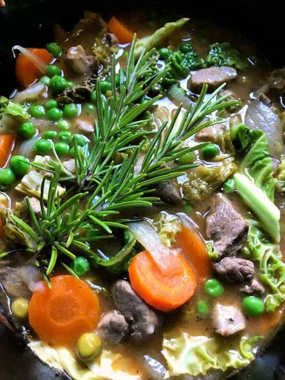 Close up of cooked lamb casserole with peas, carrots, rosemary.
