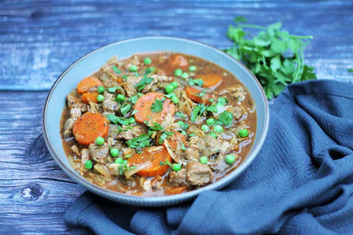 Bowl of lamb stew with herbs beside it.