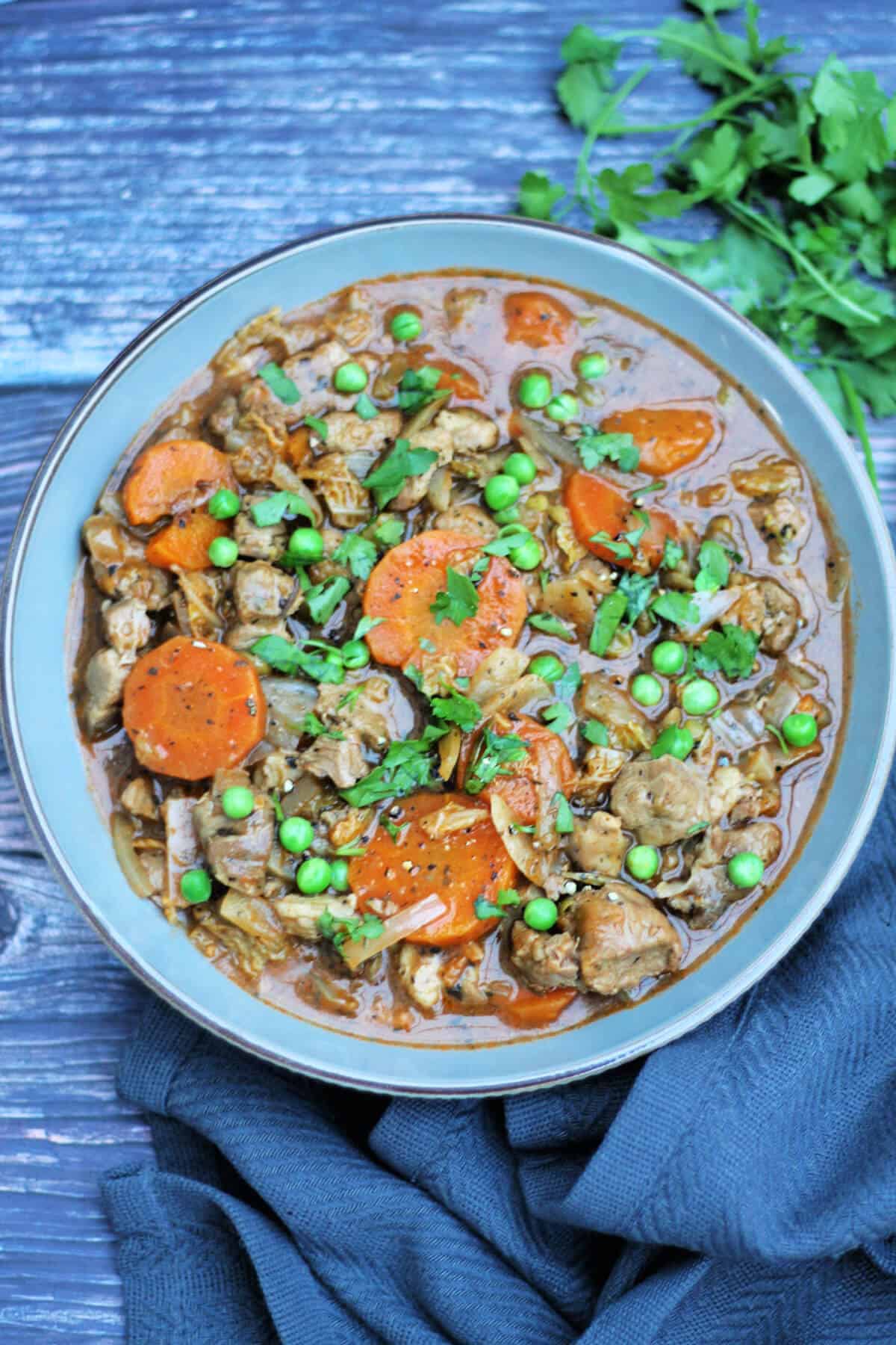 Grey bowl of lamb casserole garnished with fresh herbs, with grey cloth beside.