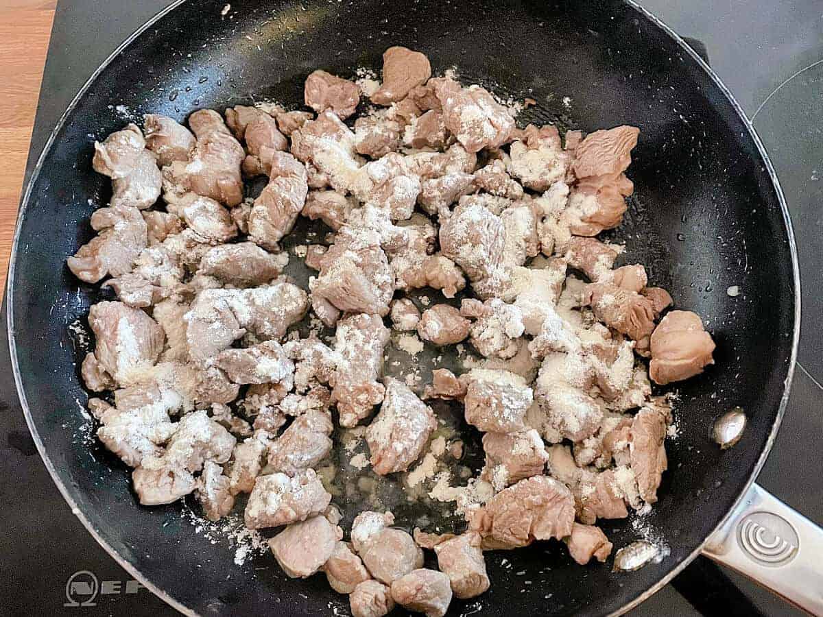 Diced lamb with flour sprinkled over it, in a saucepan.