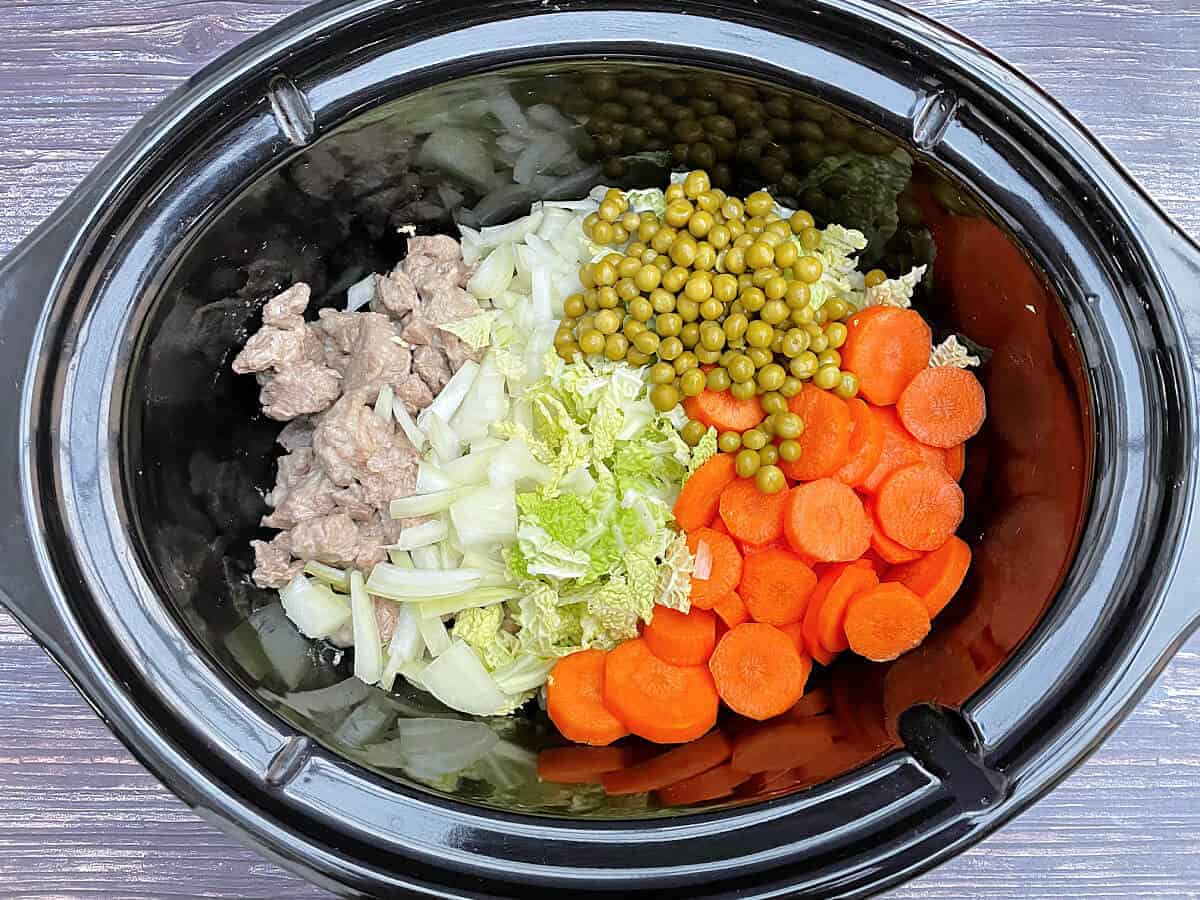 Diced lamb, onion, cabbage, carrots and peas in slow cooker pot.