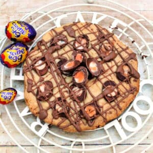 Creme egg topped shortbread with chocolate drizzle on cooling rack.