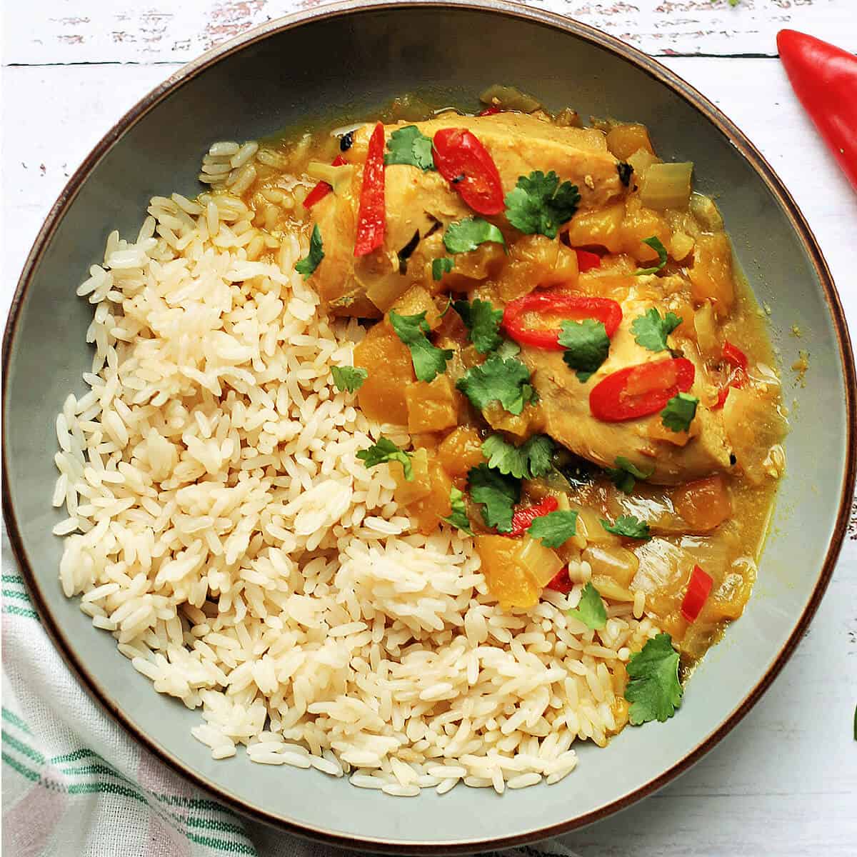 Grey bowl with chicken and mango curry with rice, with slices of red chilli and coriander leaves.