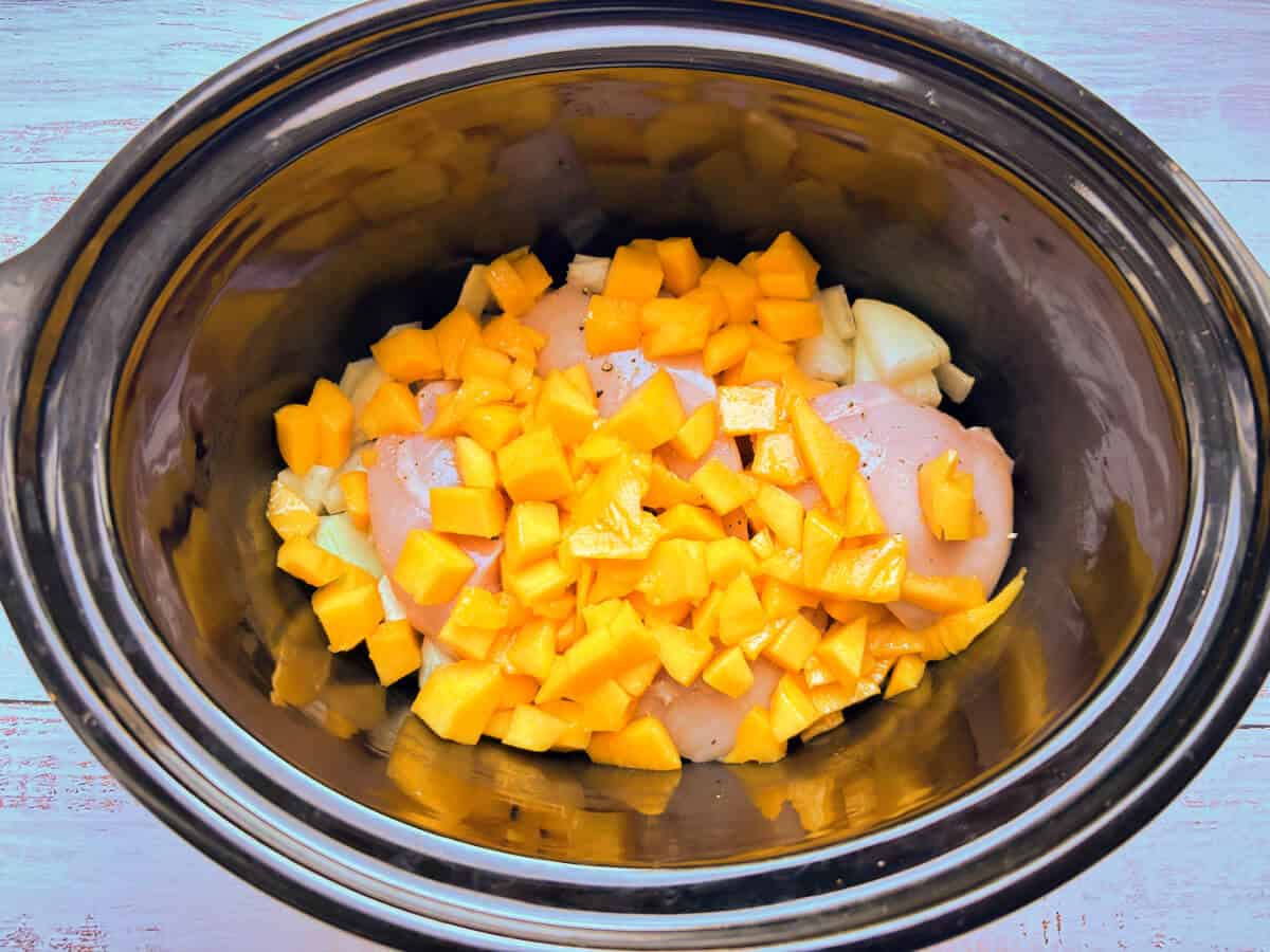 Chicken topped with diced mango in slow cooker pot.