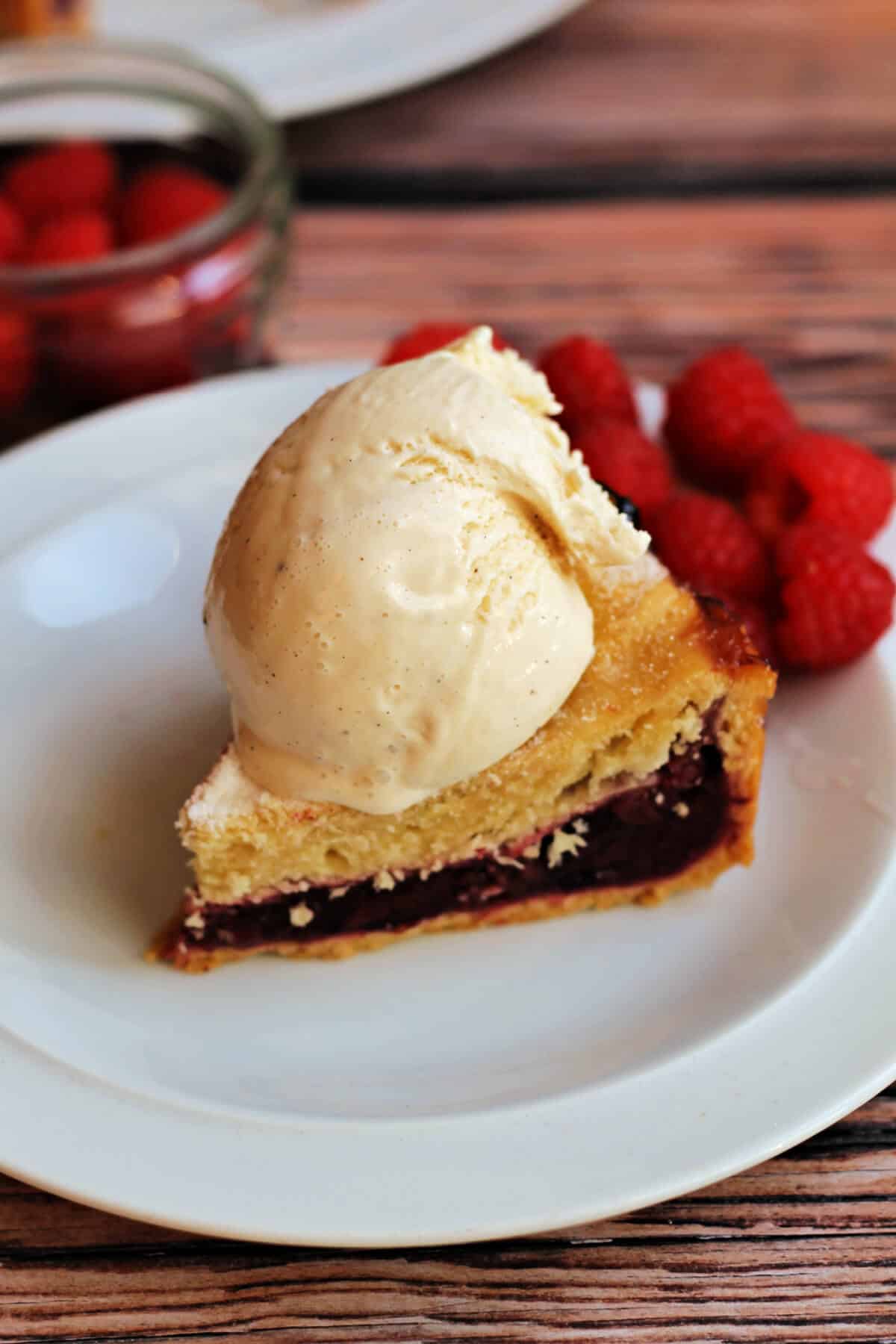 A slice of berry pie with vanilla ice cream and berries on a white plate.