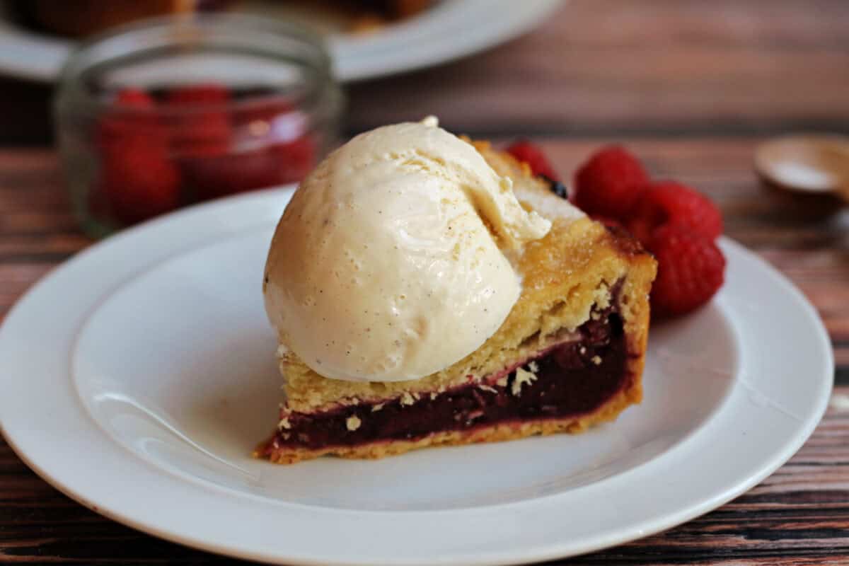 A slice of berry pie with vanilla ice cream on top on a plate.
