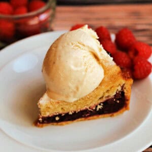 Slice of fruit pie with ice cream on top and berries on the side.