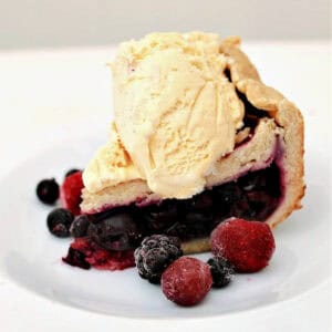 Slice of berry pie topped with ice cream on white plate.