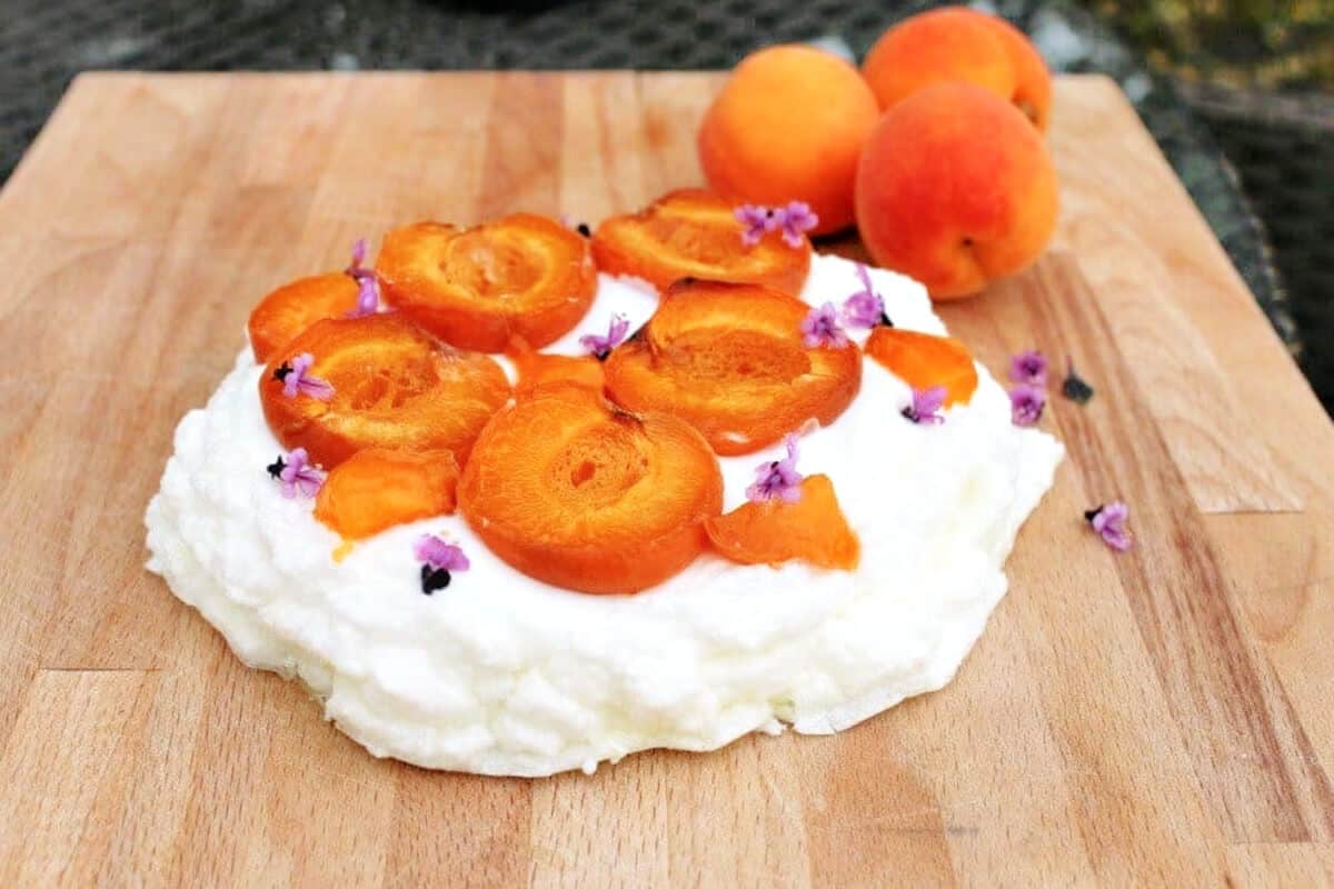 Pavlova with creamy filling and apricots on serving board.
