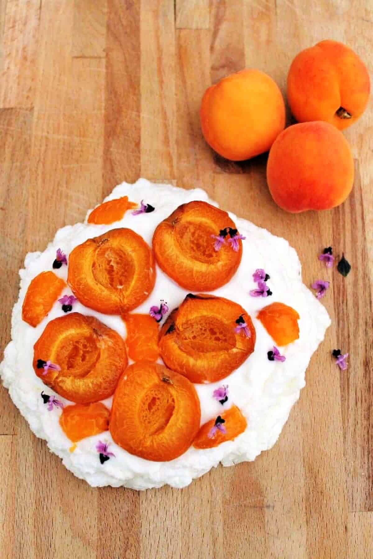 A pavlova decorated with roasted apricots on a wooden board.