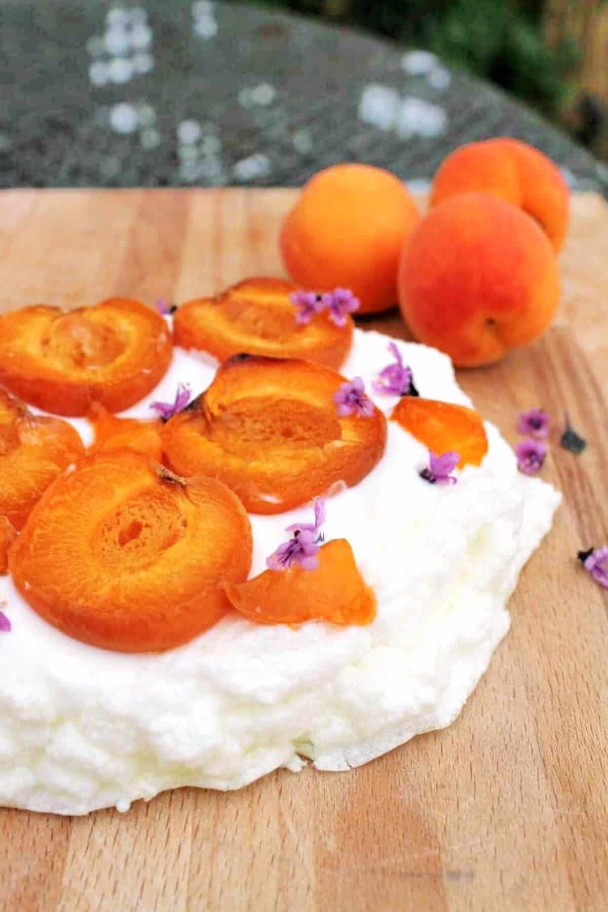 Juicy roasted apricots on a meringue, garnished with purple edible flowers.