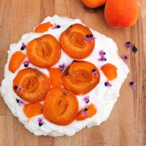 Apricot pavlova topped with halved apricots on wooden board.