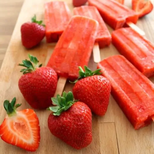 Close up of strawberry ice lollies and strawberries on a wooden board.