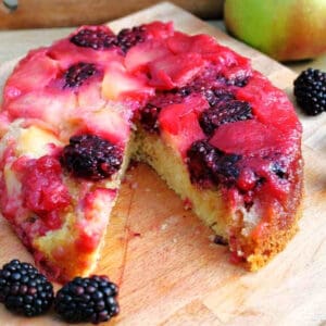 A cake topped with apple and blackberries on a wooden board.