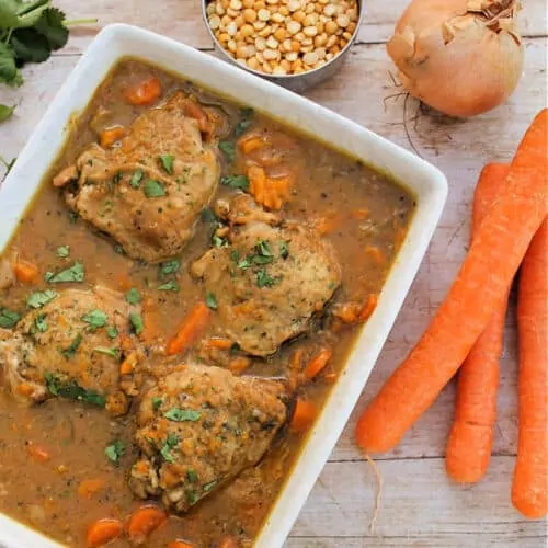 Chicken casserole in a white dish with onions and carrots to the side.