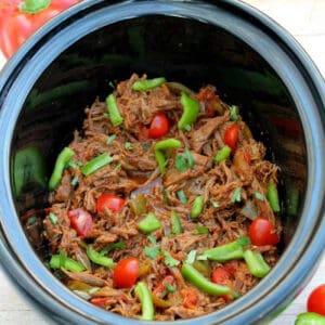 Shredded beef in the slow cooker pot with tomatoes and green peppers.