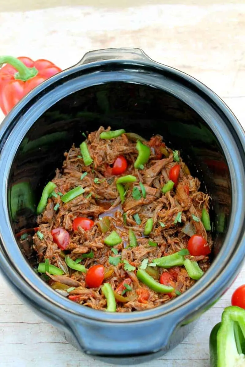 Shredded beef in a slow cooker pot with green peppers and tomatoes.