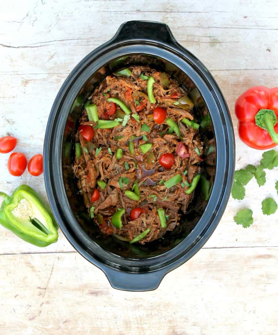 View from above of slow cooker containing shredded beef and peppers on the table next to it.