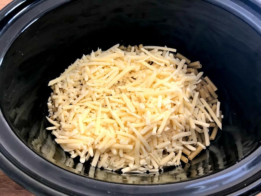 Macaroni cheese and grated cheese in slow cooker pot.
