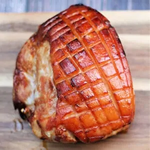 Gammon/ham with scored fat on a wooden board.