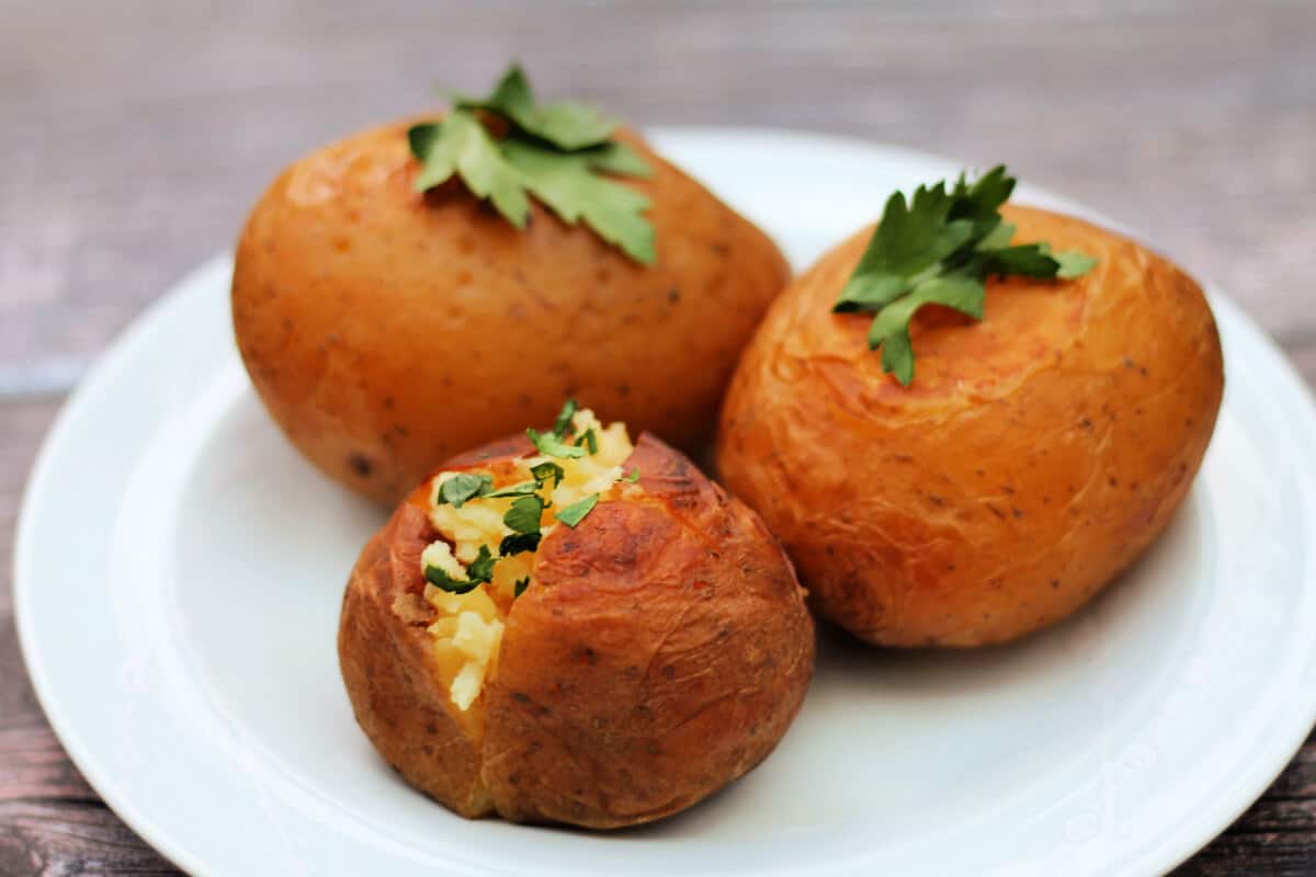 Three baked potatoes on a plate, ready to serve.