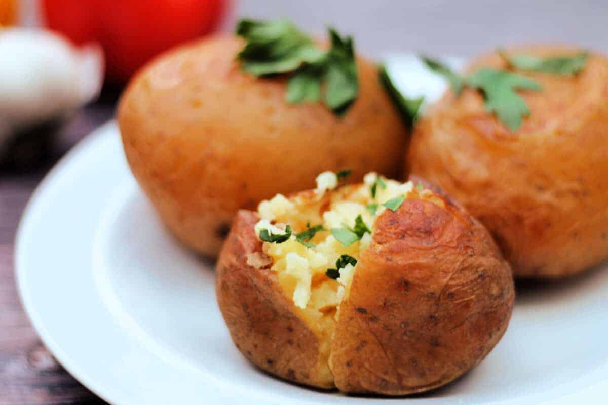 Baked potatoes split and topped with herbs on a white plate.