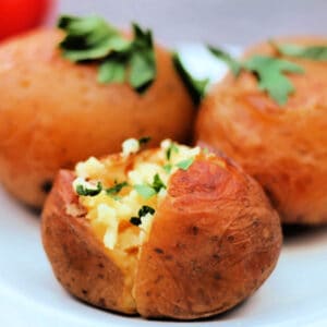 A baked potato cut open topped with fresh herbs.