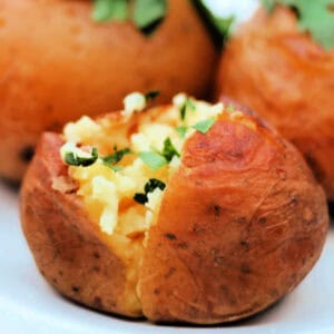 A baked potato cut open topped with fresh herbs.