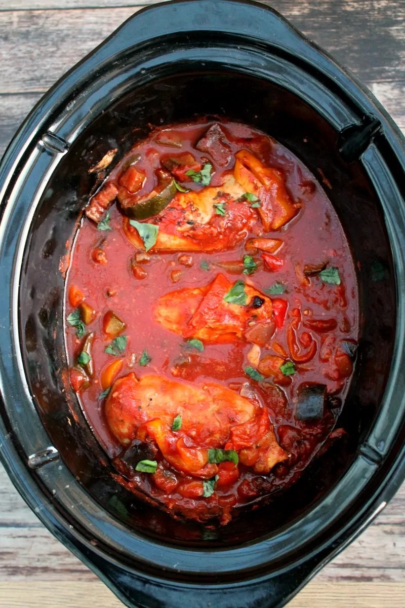 Slow cooker pot with vibrant red chicken and ratatouille stew after cooking.