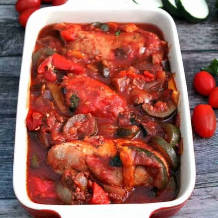 Chicken and ratatouille stew in a serving dish, with vegetables in background.