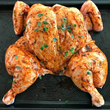 A chicken with a spice rub on an oven tray.