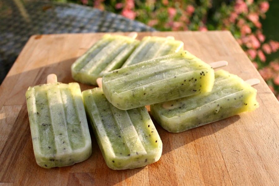 Horizontal close up of green kiwi ice lollies in a garden, on a wooden board.