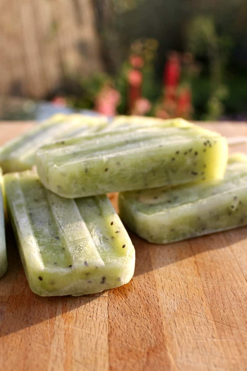 Side view of some green kiwi ice lollies on a wooden chopping board.