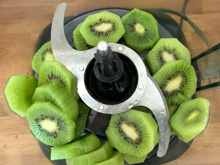 Kiwi fruit slices in a blender bowl with blade.