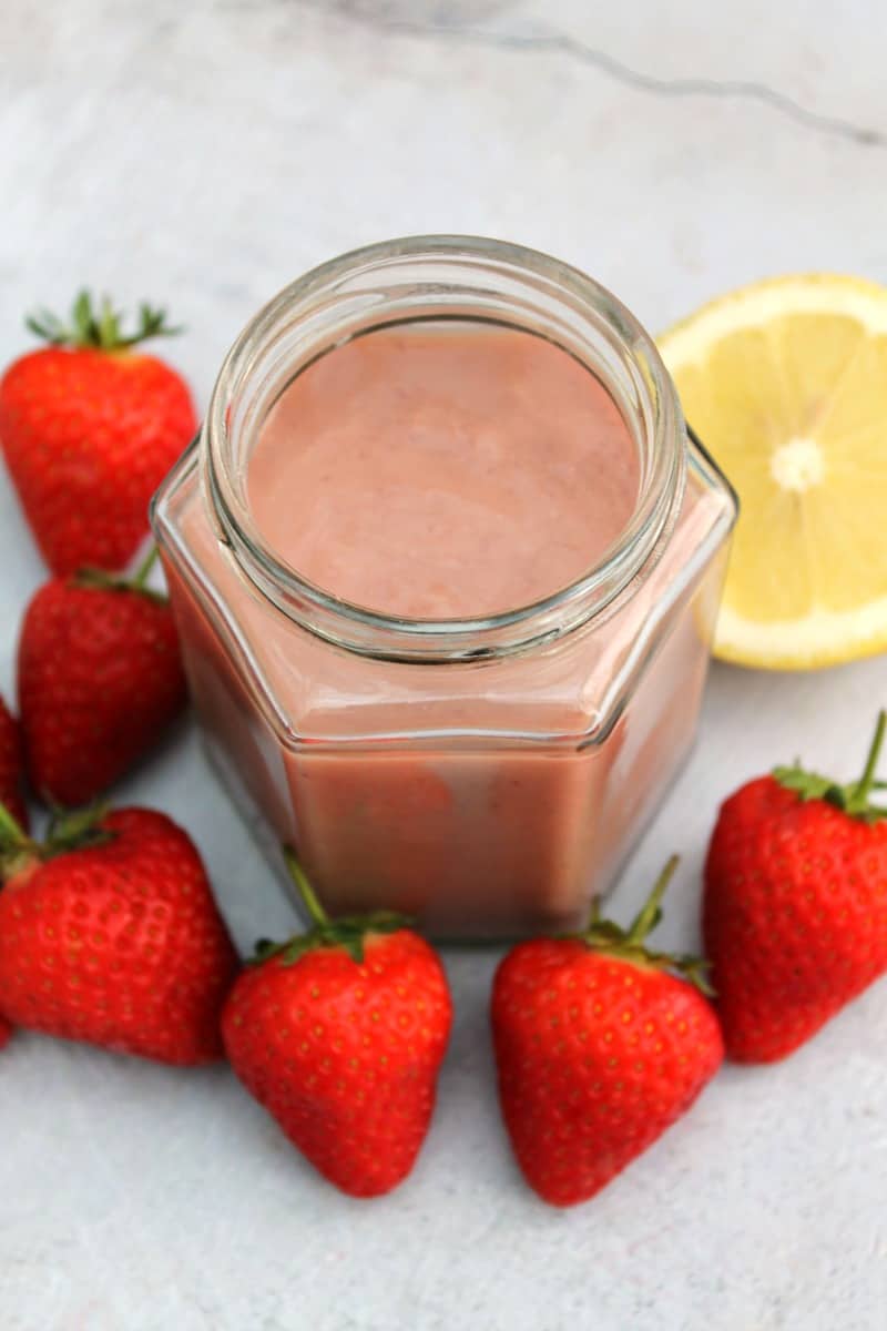 Jar of strawberry curd from above, surrounded with strawberries and a cut lemon.
